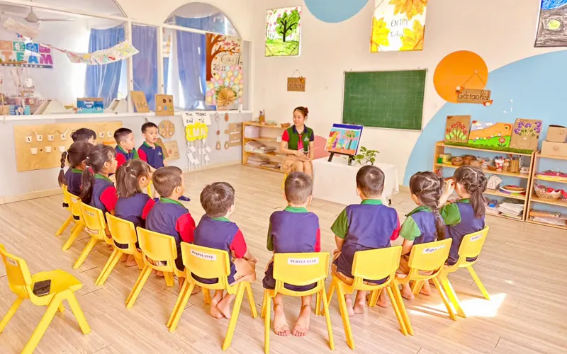 Các bé ngồi vòng tròn nghe cô giáo trong lớp buổi sáng